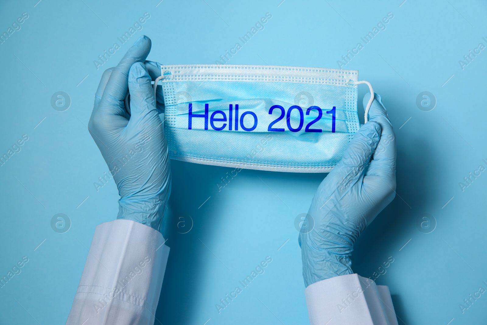 Image of Hello 2021. Doctor in gloves holding disposable face mask on light blue background, closeup