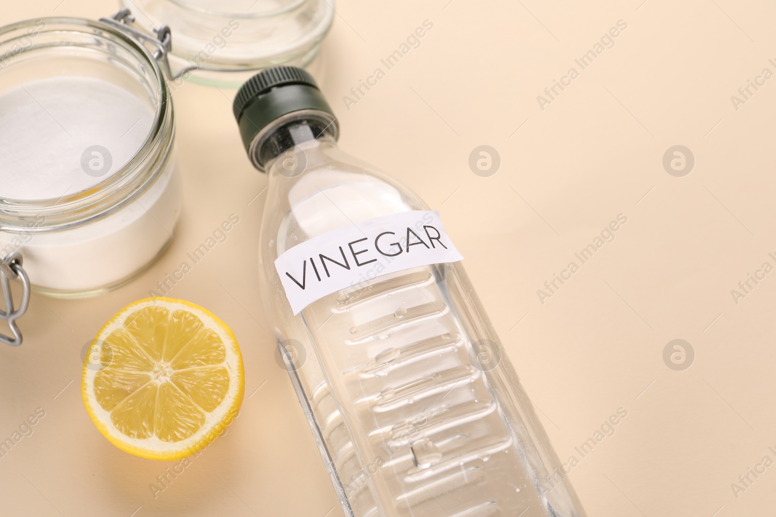 Photo of Eco friendly natural cleaners. Vinegar in bottle, cut lemon and jar of soda on beige background. Space for text