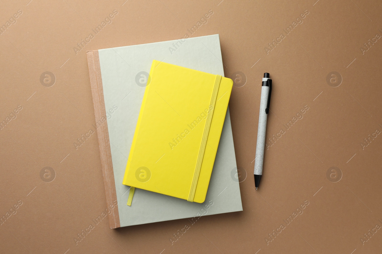 Photo of Different notebooks and pen on light brown background, top view