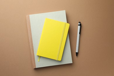 Photo of Different notebooks and pen on light brown background, top view