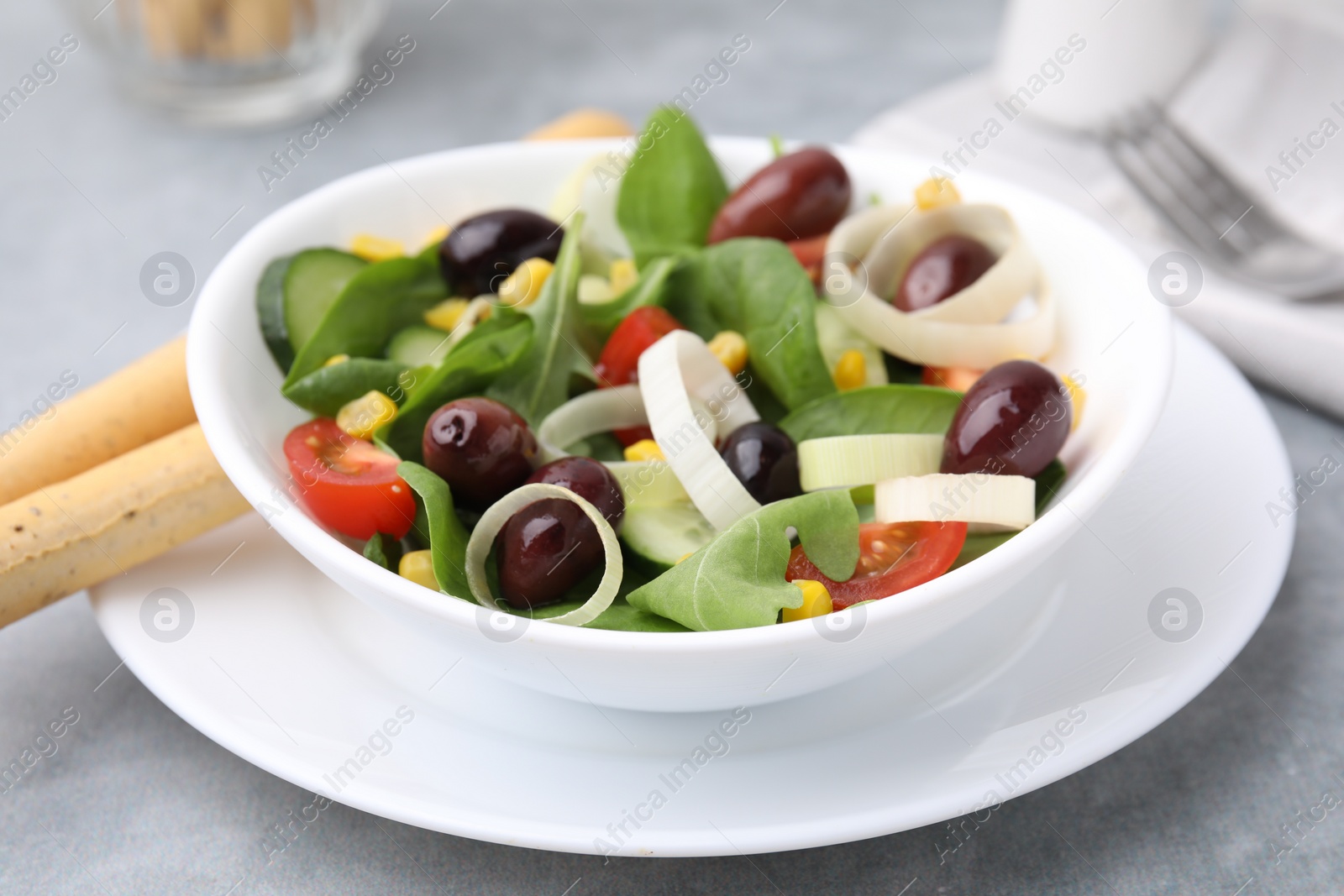 Photo of Bowl of tasty salad with leek and olives on grey table, closeup