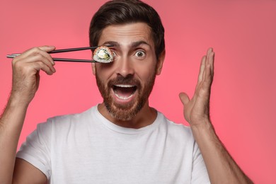 Emotional man hiding his eye with tasty sushi roll against pink background