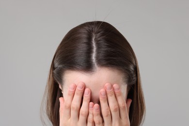 Woman suffering from hair loss problem on grey background, closeup