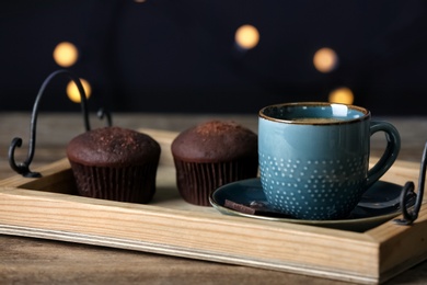 Photo of Cup of drink and chocolate muffins on wooden table against blurred lights, closeup