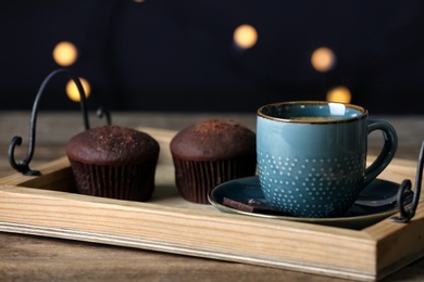 Cup of drink and chocolate muffins on wooden table against blurred lights, closeup