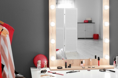 Photo of Table with makeup products and mirror near grey wall. Dressing room