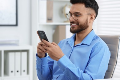 Photo of Happy young man using smartphone in office