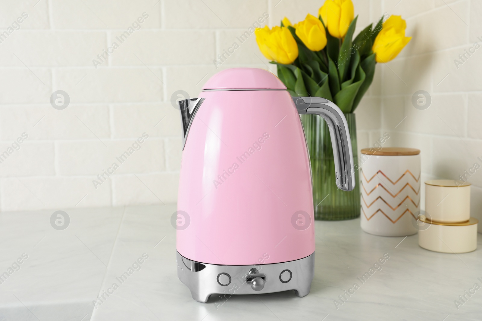 Photo of Modern electric kettle and bouquet on counter in kitchen