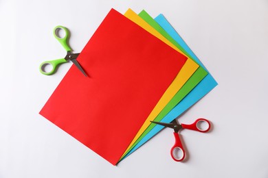 Scissors and color sheets of paper on white background, flat lay