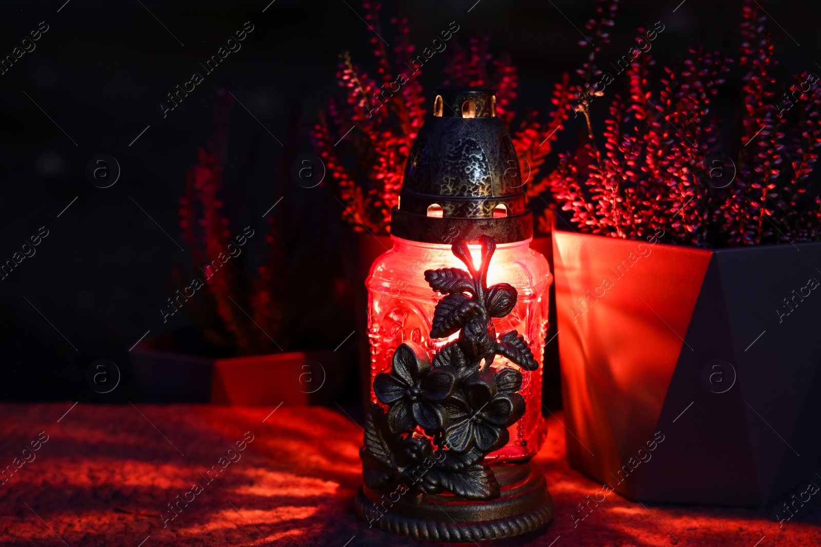 Photo of Grave lantern with burning candle on stone surface at night