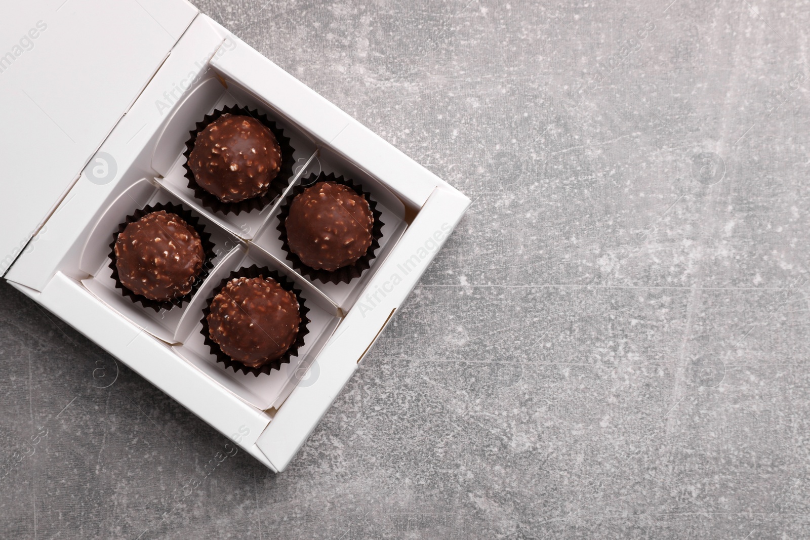 Photo of Delicious chocolate candies in box on light grey table, top view and space for text