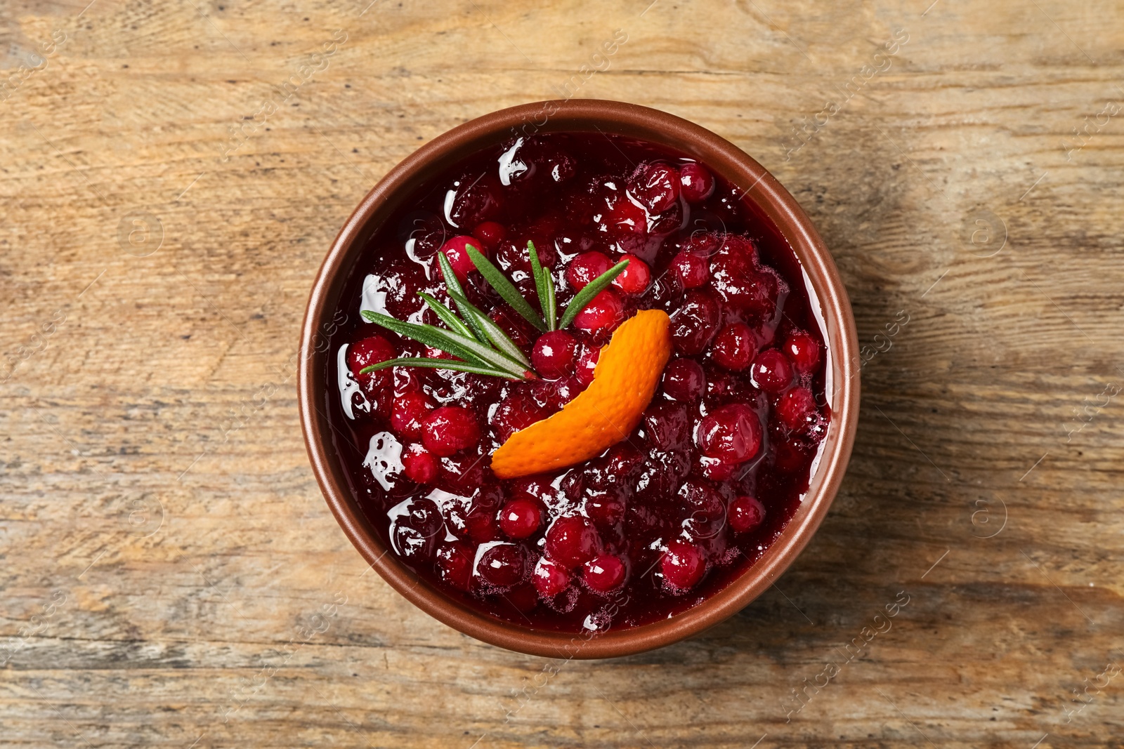 Photo of Cranberry sauce with orange peel and rosemary on wooden table, top view