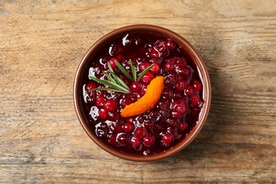 Photo of Cranberry sauce with orange peel and rosemary on wooden table, top view