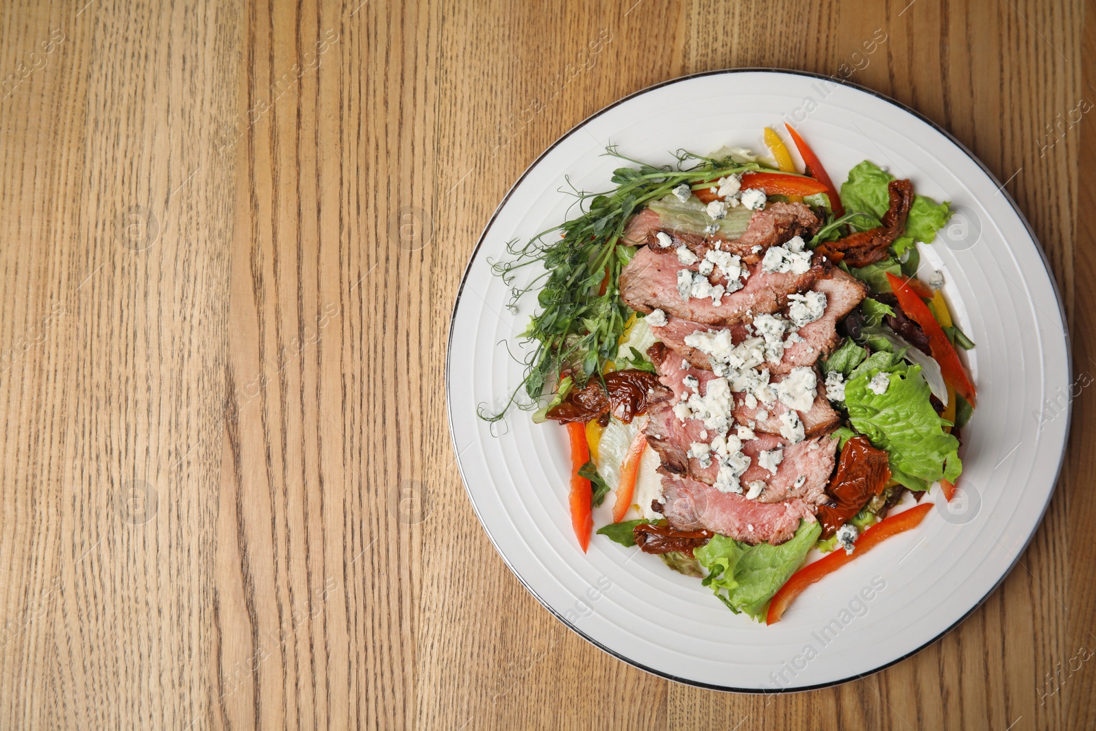 Photo of Delicious salad with roasted meat and vegetables served on wooden table, top view. Space for text