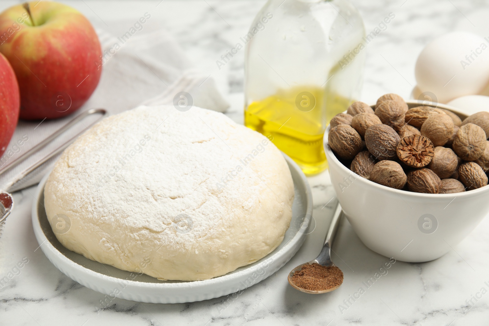 Photo of Raw dough, nutmeg seeds and other ingredients for pastry on white marble table, closeup