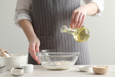 Photo of Woman pouring oil into bowl at white wooden table indoors, closeup. Cooking traditional grissini