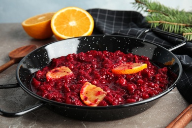 Photo of Tasty cranberry sauce with citrus fruit slices in pan on table