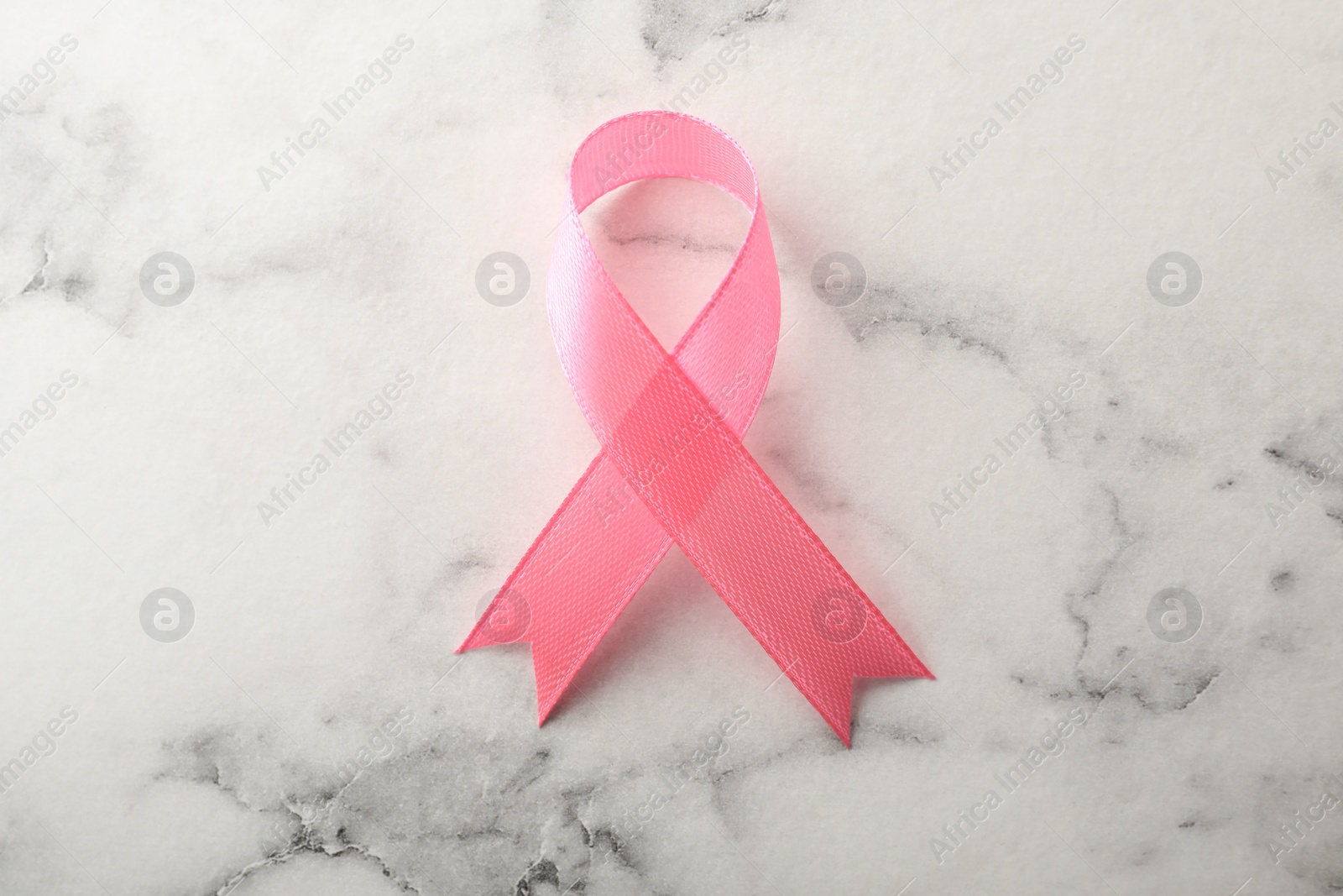 Photo of Pink ribbon on marble background, top view. Breast cancer awareness concept