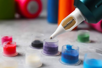 Photo of Dipping tattoo machine needle into ink on light grey table, closeup