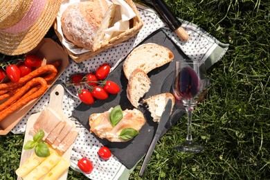 Photo of Blanket with wine and snacks for picnic on green grass, flat lay