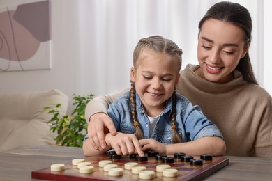 Playing checkers. Mother learning her daughter at table in room