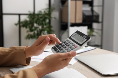 Woman using calculator at table in office, closeup