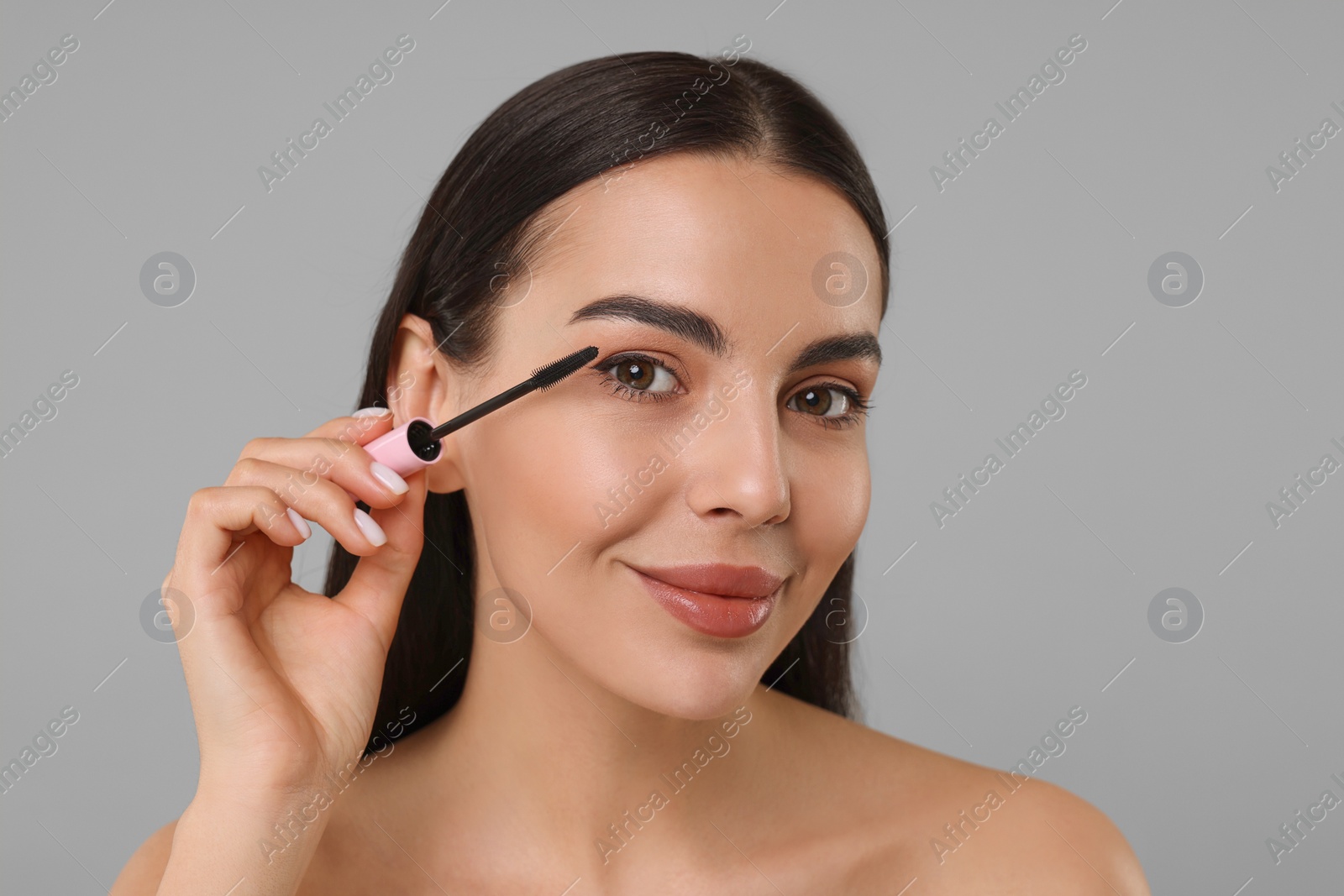 Photo of Beautiful young woman applying mascara on grey background