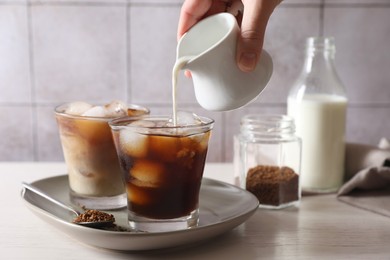 Photo of Woman pouring milk into glass with refreshing iced coffee at light table, closeup