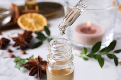 Photo of Dropping anise essential oil from pipette into bottle on table, closeup