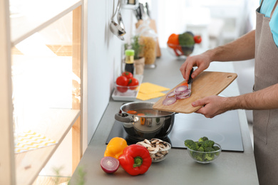 Young man cooking delicious vegetable soup in kitchen, closeup