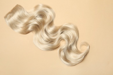 Lock of blonde wavy hair on color background, top view