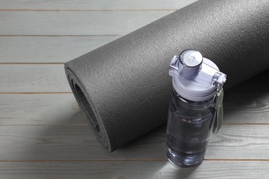 Photo of Yoga mat and bottle of water on grey wooden floor