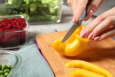 Photo of Woman cutting bell pepper and containers with fresh products on table, closeup. Food storage