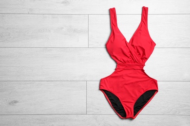 Photo of One-piece swimsuit on wooden background, top view