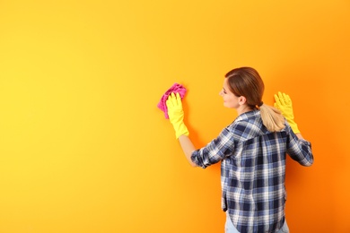 Photo of Young woman cleaning color wall with rag