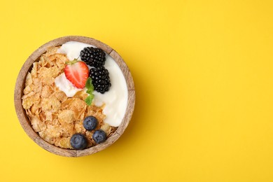 Delicious crispy cornflakes, yogurt and fresh berries in bowl on yellow background, top view with space for text. Healthy breakfast