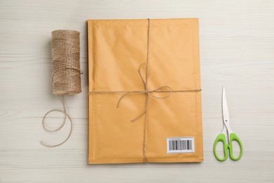 Padded envelope, rope and scissors on white wooden background, flat lay