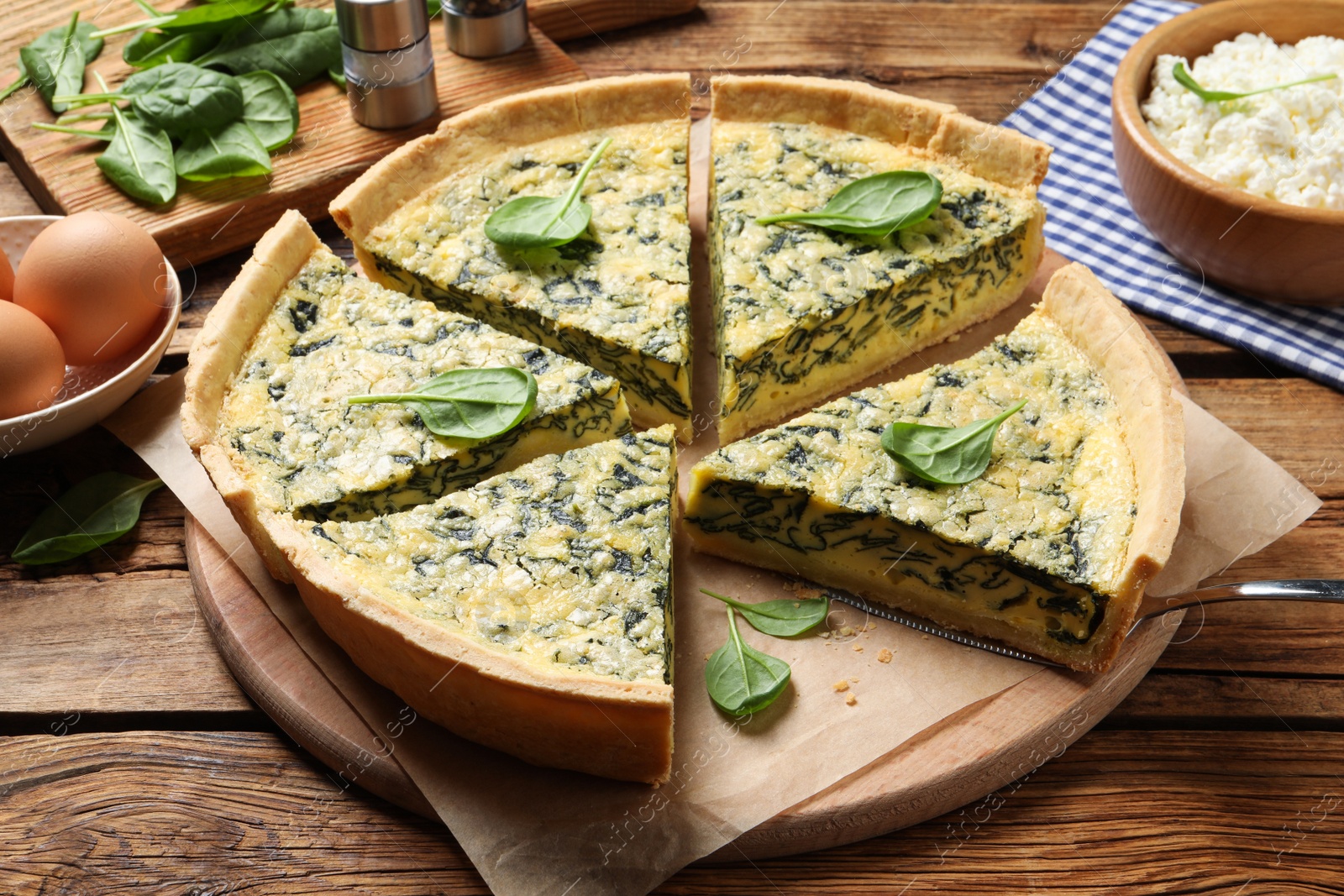 Photo of Cut delicious spinach pie with ingredients on wooden table