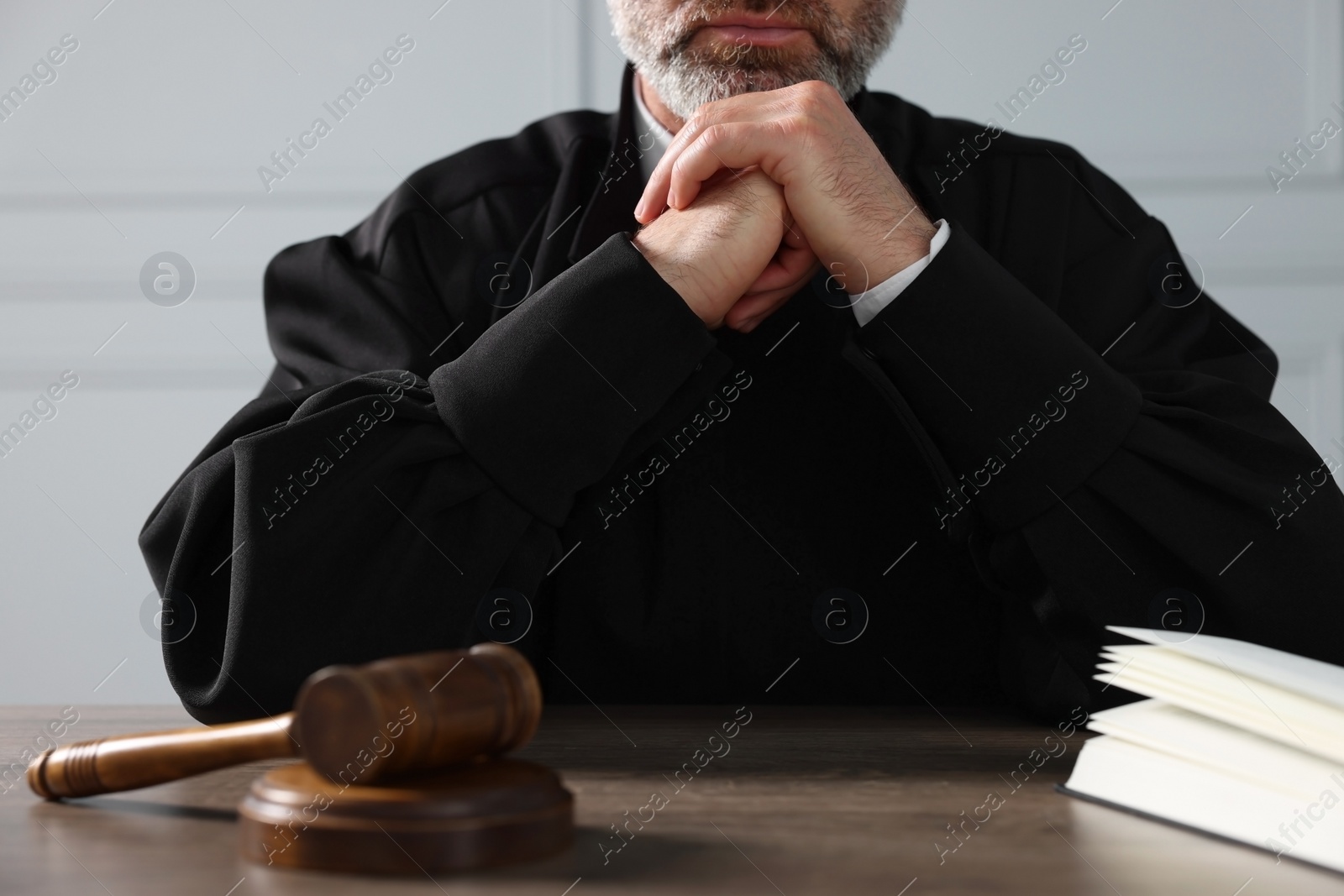 Photo of Judge with gavel and book sitting at wooden table indoors, closeup