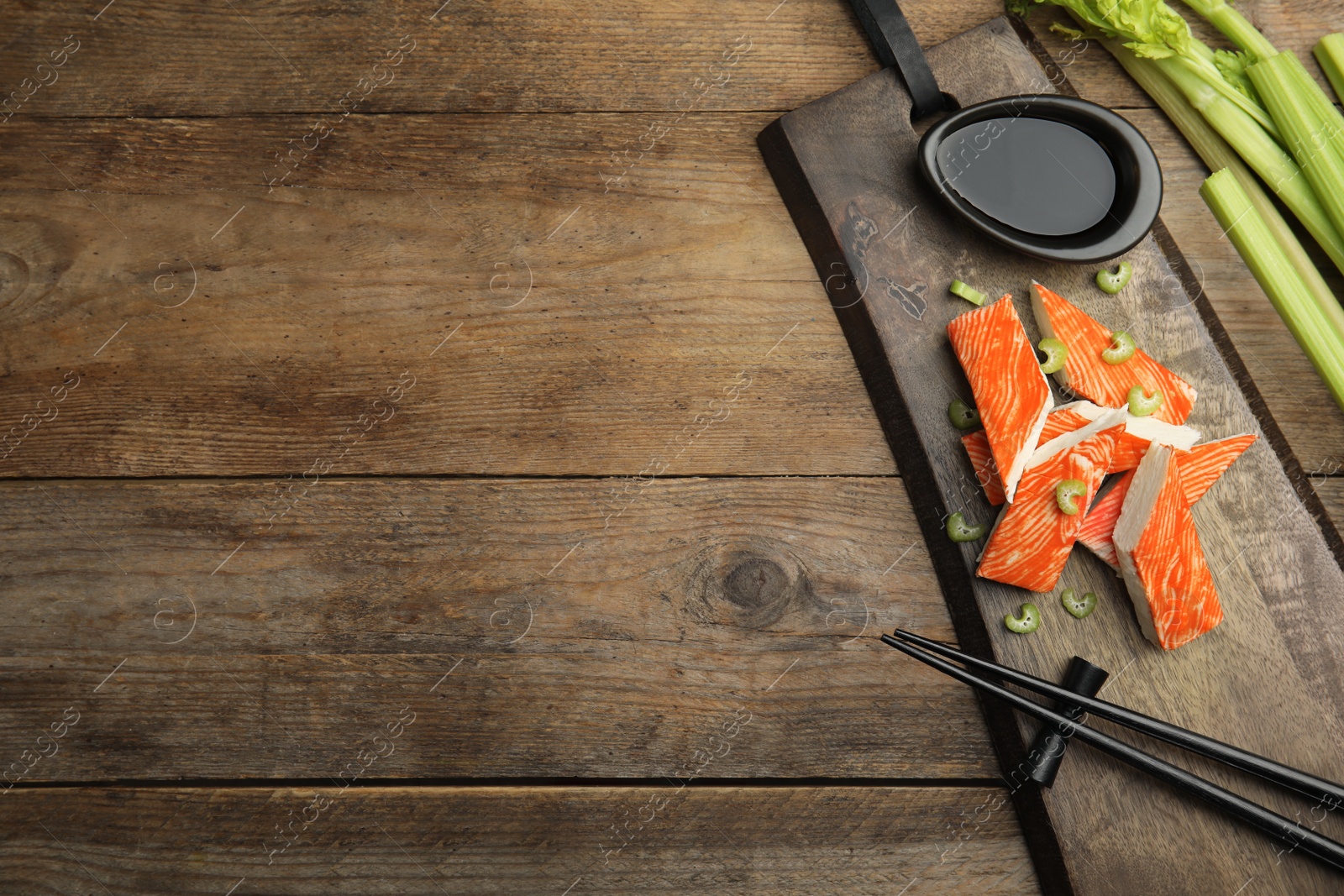 Photo of Fresh crab sticks with celery and soy sauce served on wooden table, flat lay. Space for text