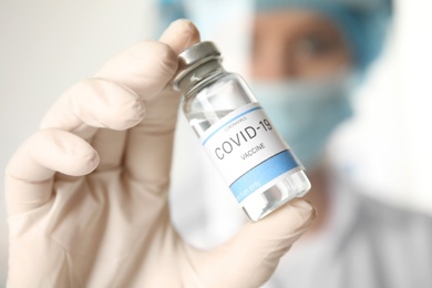 Doctor holding vial with vaccine against Covid-19 on light background, closeup