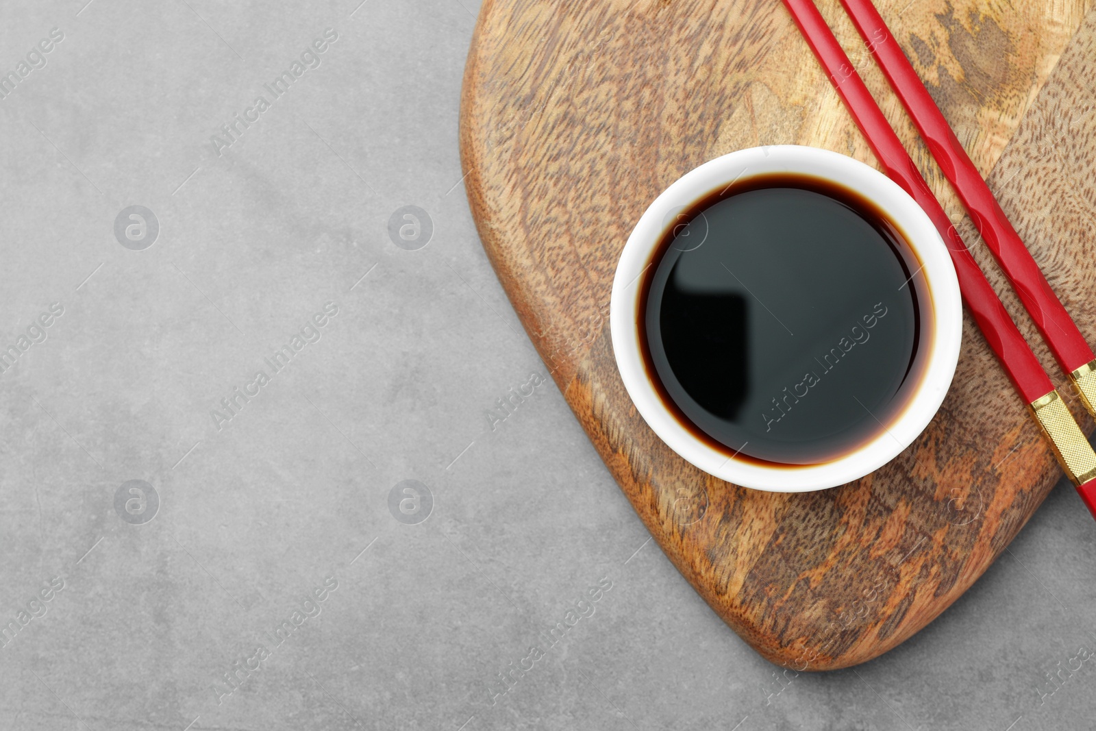 Photo of Bowl of soy sauce and chopsticks on grey table, top view. Space for text