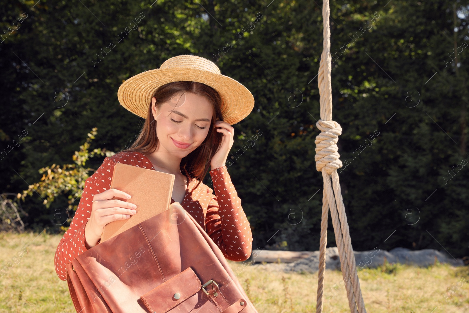 Photo of Beautiful young woman taking book from bag outdoors on sunny day. Space for text