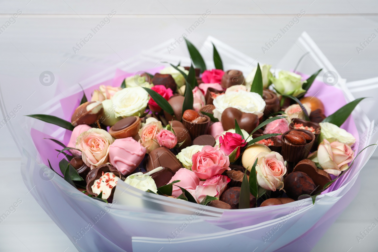 Photo of Beautiful bouquet of flowers and chocolate candies on light background, closeup