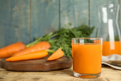 Glass of freshly made carrot juice on wooden table, space for text