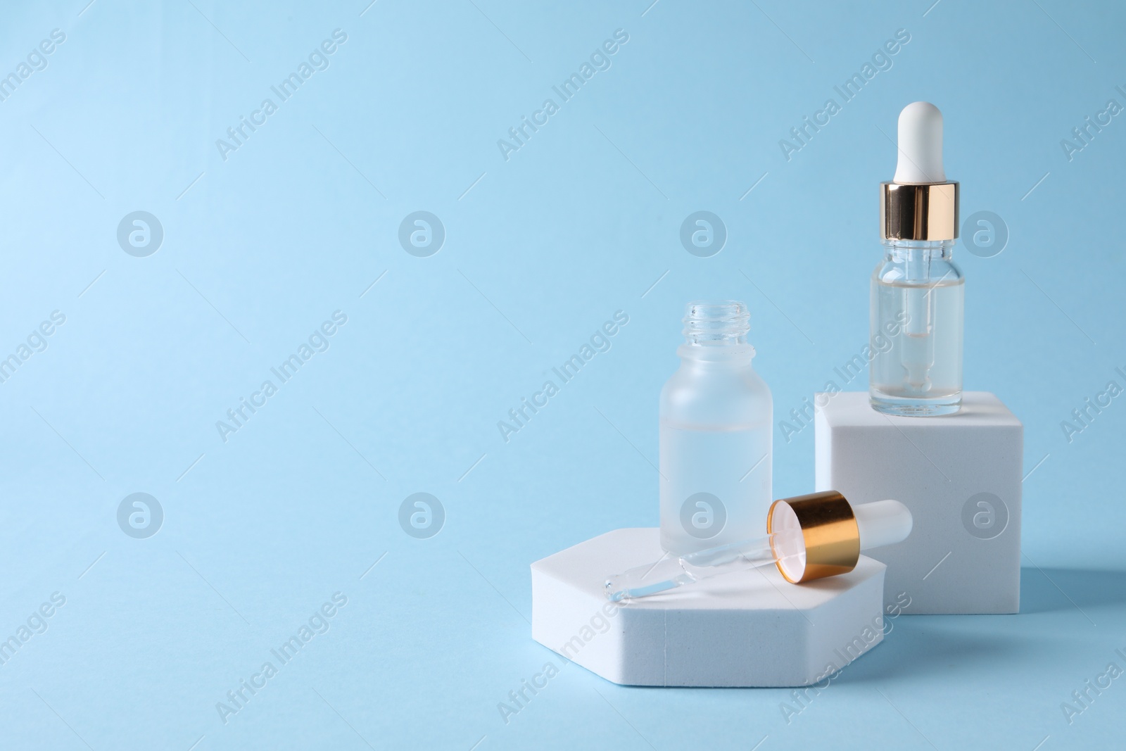 Photo of Presentation of bottles with cosmetic serums on light blue background, space for text