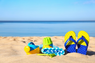 Photo of Beautiful view of sand with plastic beach toys and flip flops near sea on sunny day. Space for text