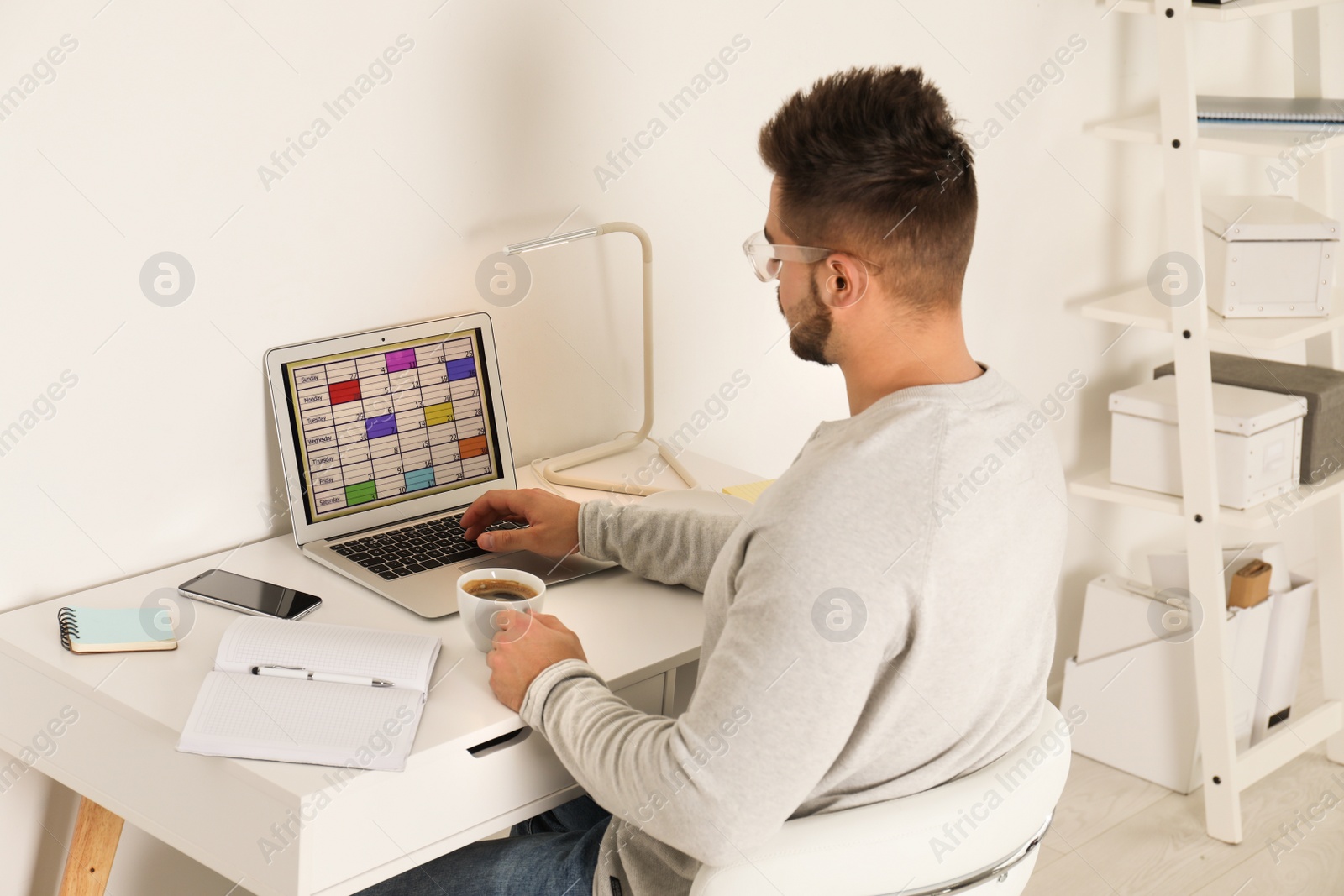 Photo of Young man using calendar app on laptop in office