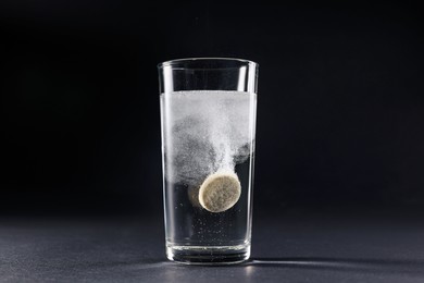 Photo of Effervescent pill dissolving in glass of water on grey table