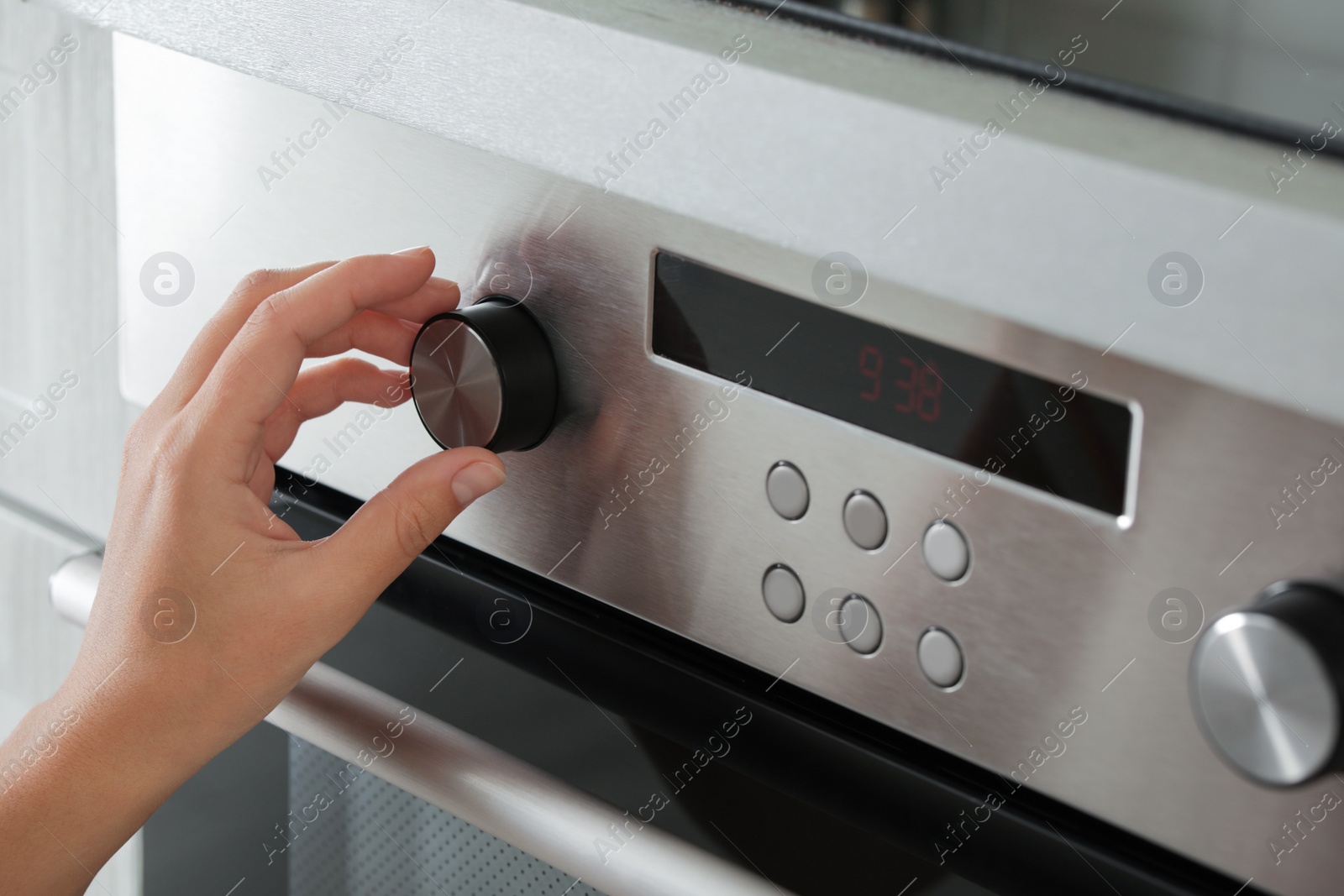 Photo of Woman regulating cooking mode on oven panel, closeup